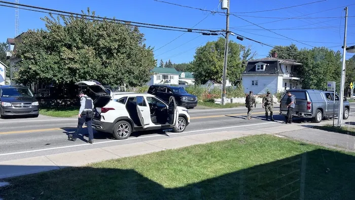 一名警察在村庄街道上绕过一辆车门和后备箱全部打开的越野车。