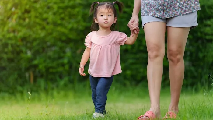 一个中国幼儿牵着一位女士的手在草坪上散步。